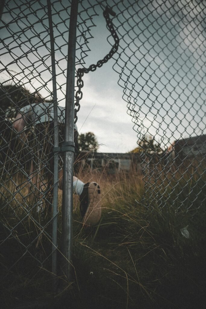 pexels-photo-2953898-2953898 A person exploring an abandoned area through a broken chain link fence.